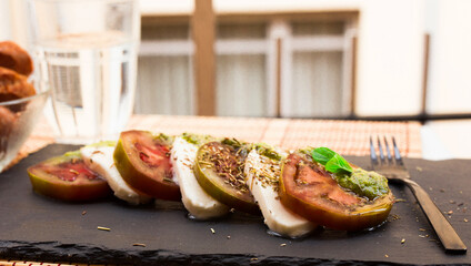 Caprese salad with mozzarella, black tomatoes and pesto on black stone plate