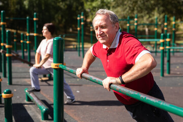 Elderly man doing exercises on a horizontal bar at an outdoor sports ground