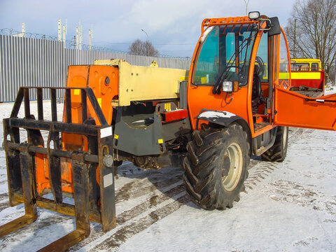 Orange forklift loader with extended attachment on a snowy construction site.