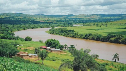Obraz premium River flows through rural African landscape, village visible, hills in background; tourism