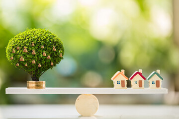 Home model and money bag of tree with growing with investment put on the stack gold coin put on the wood scales in the public park, Real estate and business investment concept.