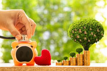 Man hand use a stethoscope with check hygiene of sick piggy bank and red heart and stack gold coin with growing and money bag of tree  in the public park, Saving for buy health insurance concept.