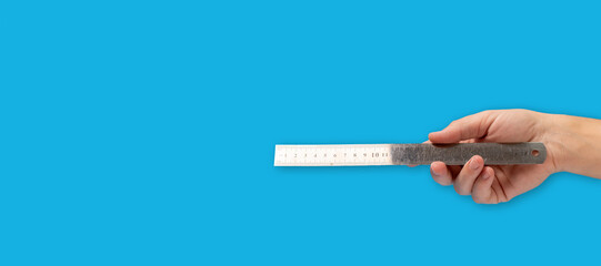 Hand holding metal ruler on blue background with copy space.