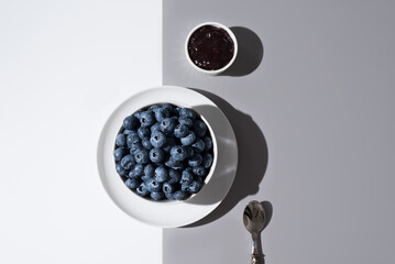 Arándanos en un recipiente blanco y mermelada de arándanos sobre un fondo gris y blanco. Vista superior	