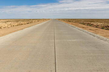 Long concrete road stretches through the vast landscape of Karakalpakstan in Uzbekistan