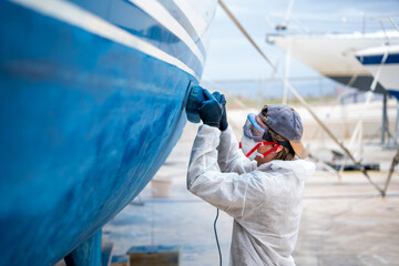 a man polishing the side of the hull of a blue ship.