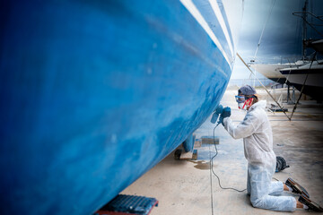 a man polishing the side of the hull of a blue ship.