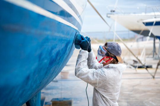 a man polishing the side of the hull of a blue ship.