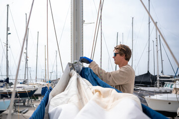 A young white man repairing the mainsail of a catamaran. Maintenance issue.