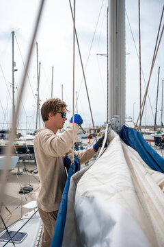 A young white man repairing the mainsail of a catamaran. Maintenance issue.