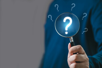 Close-up of a hand holding a magnifying glass with question marks in the background, symbolizing...