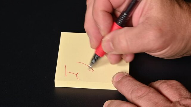 Valentine's Day concept. A yellow office sticky note (Post-it). A hand holding a red pen writes the phrase "I Love You" and then flips the note, which becomes illuminated by light, making the text cle