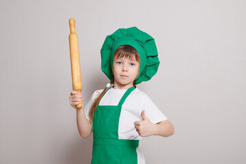 A cute little girl in a chef's costume with a rolling pin in his hands