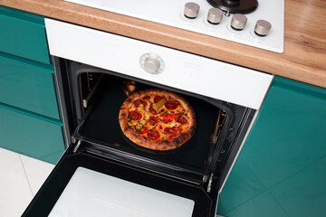 Baked pizza with sausage and pepper in the oven in the green kitchen. Cooking. Restaurant advertising banner. Italian, spicy. Homemade food.