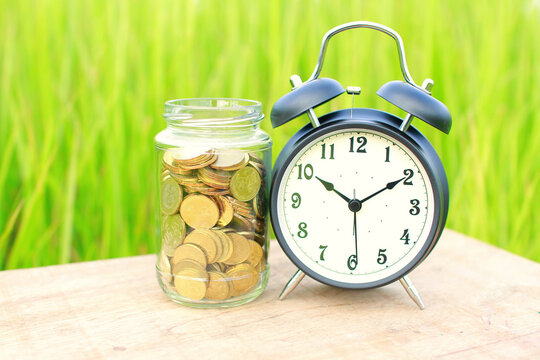 Close-up of an old-fashioned Alarm clock on a table next to a jar filled with coins