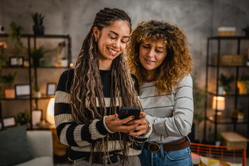 two female friends use mobile phone and have fun together at home