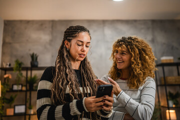 two female friends use mobile phone and have fun together at home