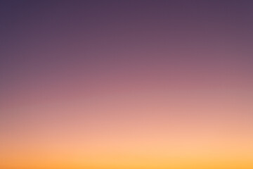 Clear sunset sky background. Vibrant gradient from orange to purple. Beautiful and natural color transient without any clouds. Real sky view.