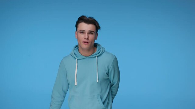 young rapper in blue hoodie signing and making gang gestures at camera while moving on blue background