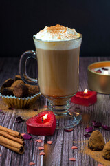 A glass of Viennese coffee with cream, cinnamon in a romantic setting with candles, sweets on a dark wooden background. Valentine's Day..