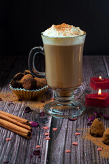 Glass of coffee with cream, cinnamon in a romantic setting with candles on a dark wooden background. Valentine's Day.