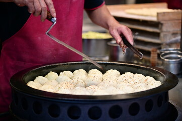 In this image, a vendor carefully picks up hot shuijianbao from the pan. The golden crust and steaming filling highlight why this dish is a Taiwanese night market staple.
