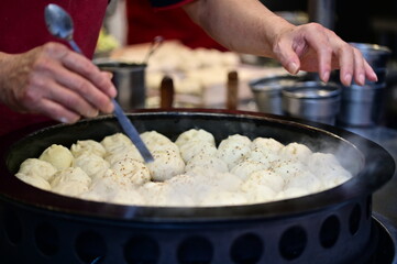 The art of cooking shuijianbao lies in precise timing. Here, the vendor uses a spoon to ensure the buns achieve their signature crispy exterior and flavorful filling.
