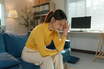 Young woman suffering from strong migraine, touching her temples, sitting on sofa in living room