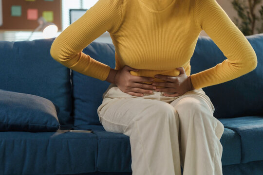 Young woman suffering from strong abdominal pain while sitting on sofa at home