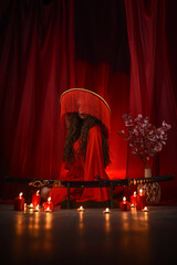 Beautiful young girl in a red kimono dress with a katana on red curtains background..