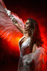 Naklejka premium Blonde girl in a white body suit with angel wings posing on fiery smoke background.