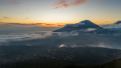 Mount Batur in Bali emerges majestically from a sea of clouds at sunrise, casting a dramatic silhouette against the vibrant sky.