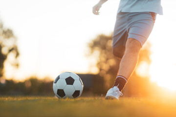 Soccer player with a ball. Action sport outdoors playing football for exercise at green grass field under the twilight sunset.