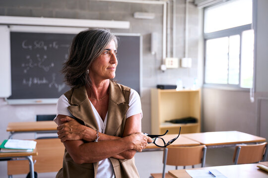 A teacher stands alone in an empty classroom, gazing thoughtfully out of the window. The scene captures a moment of reflection, introspection, and quiet contemplation in an educational setting