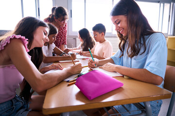 Female primary school teacher explaining in class to diverse group of students sitting at desks together. Young woman tutoring of elementary academy children gathered in the study hall. Back to school