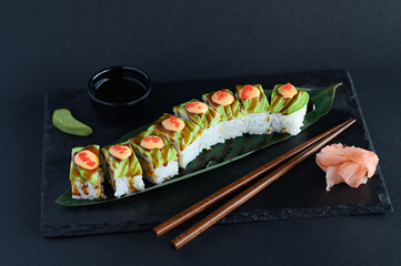 A set of sushi rolls on a wooden board and banana leaf, served with soy sauce, wasabi, ginger, and chopsticks. Perfect for an Asian restaurant menu.