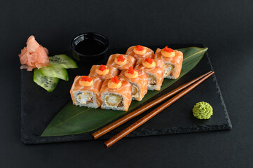 A set of sushi rolls on a wooden board and banana leaf, served with soy sauce, wasabi, ginger, and chopsticks. Perfect for an Asian restaurant menu.