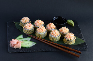 A set of sushi rolls on a wooden board and banana leaf, served with soy sauce, wasabi, ginger, and chopsticks. Perfect for an Asian restaurant menu.