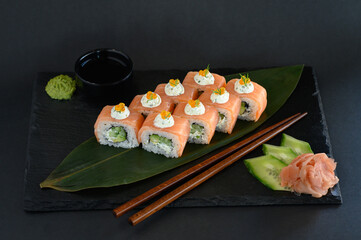 A set of sushi rolls on a wooden board and banana leaf, served with soy sauce, wasabi, ginger, and chopsticks. Perfect for an Asian restaurant menu.