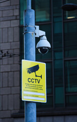 cctv video camera and warning sign on a post in the city