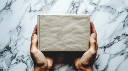 Hands gently hold a neatly wrapped small parcel against a marble surface. This evocative moment reflects the joy and anticipation of giving gifts, personal connections and surprises. Copy space