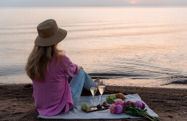 Summer picnic on the beach, bakery, fruits. Blond woman in hat. Rest time, sunset, nature