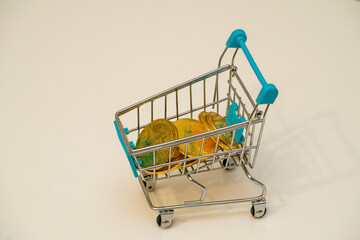 Small shopping cart filled with coins on a plain background