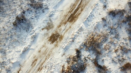 Aerial view of muddy winter road amidst snow-covered landscape.