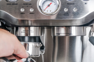 Barista hand holds a metal portafilter holder for grinded coffee beans in a coffee machine, close-up. making espresso coffee concept.
