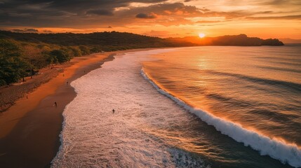 Aerial view of sunset over sandy beach with waves rolling ashore.