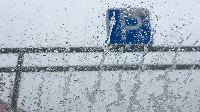 view on the parking sign through the car windshield, covered with rain and wet snow, dull grey sky background, mood of loneliness and depression
