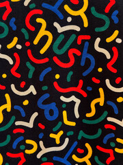 Close up pattern of confetti printed on a fabric or wallpaper. Colorful abstract confetti paper shapes scattered randomly on a black background. Suitable for kids. Seamless background texture.