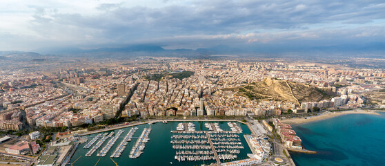 Aerial perspective of Alicante city. Panoramic view of city and port area. Famous travel destination in Spain. Yachts and boats docked. Sunset point with pink reflection on buildings and mountain. 