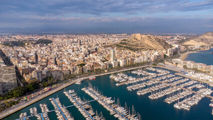 Aerial perspective of Alicante city. Panoramic view of city and port area. Famous travel destination in Spain. Yachts and boats docked. Sunset point with pink reflection on buildings and mountain. 